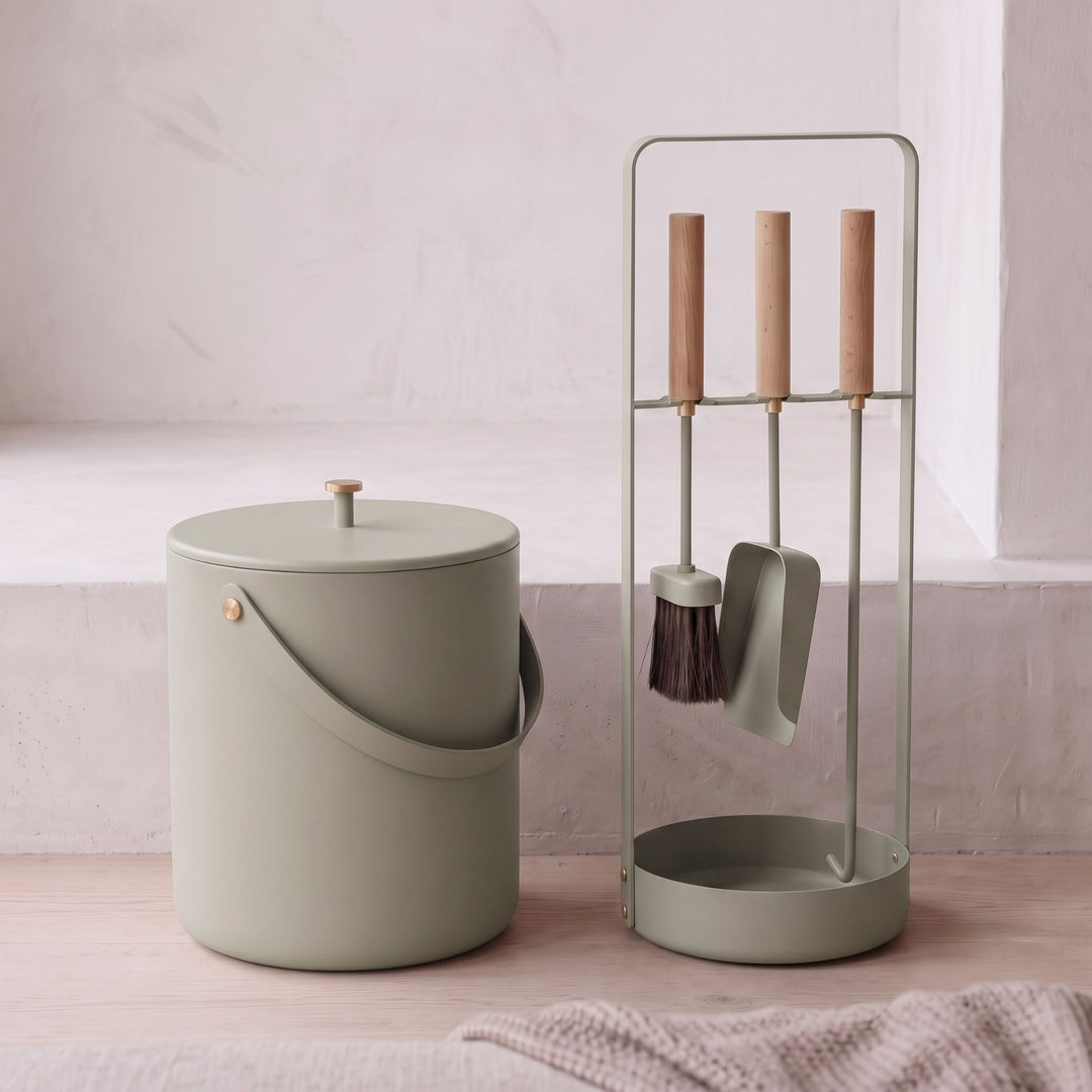 Sage green cylindrical trash can with lid and handle by IKEA, paired with matching stand holding brush, dustpan, and tools, minimalist design on wooden floor.