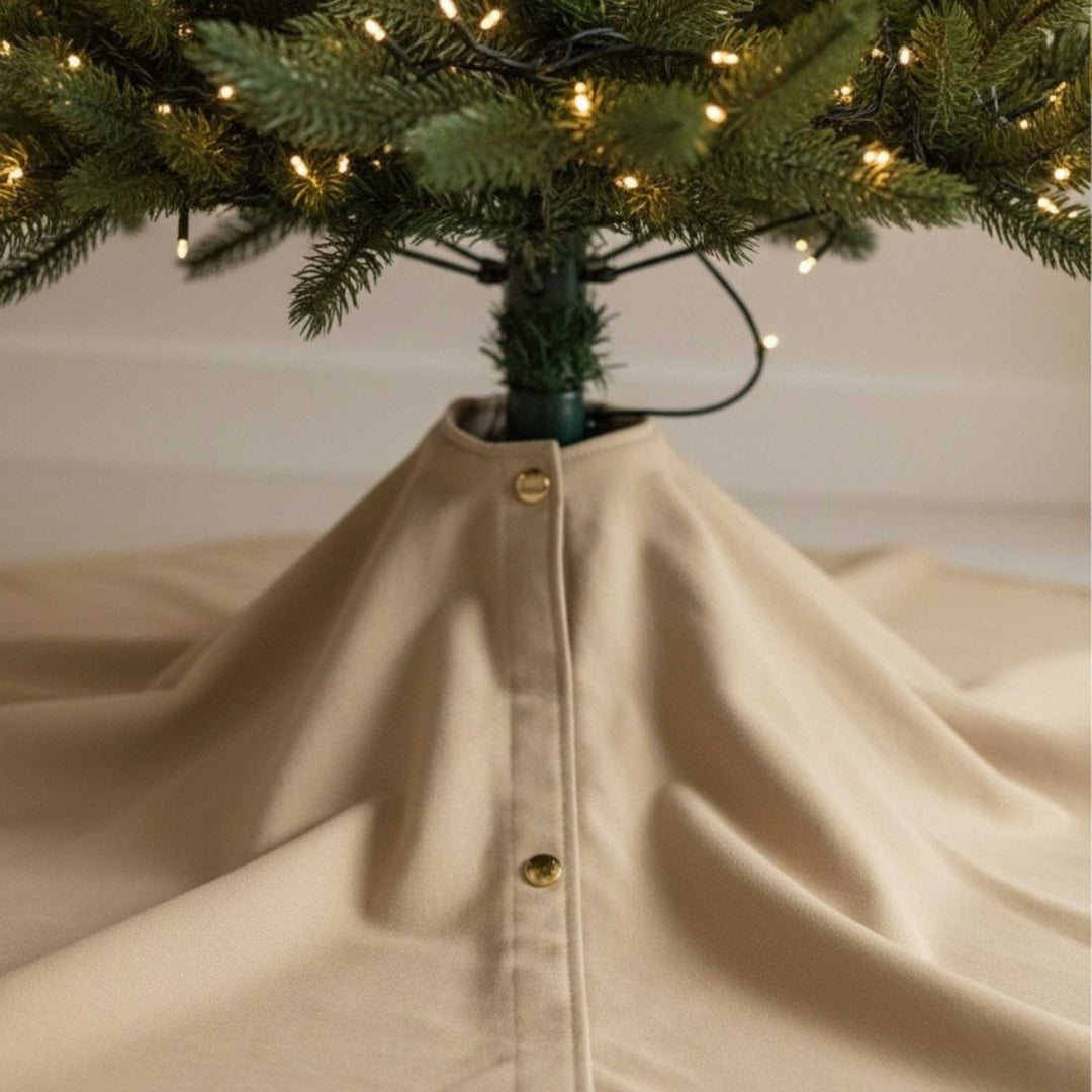 Beige Weihnachtsbaumdecke 2in1 von LIVLIG, mit Knopfleiste und glattem Stoff unter einem geschmückten Weihnachtsbaum.
