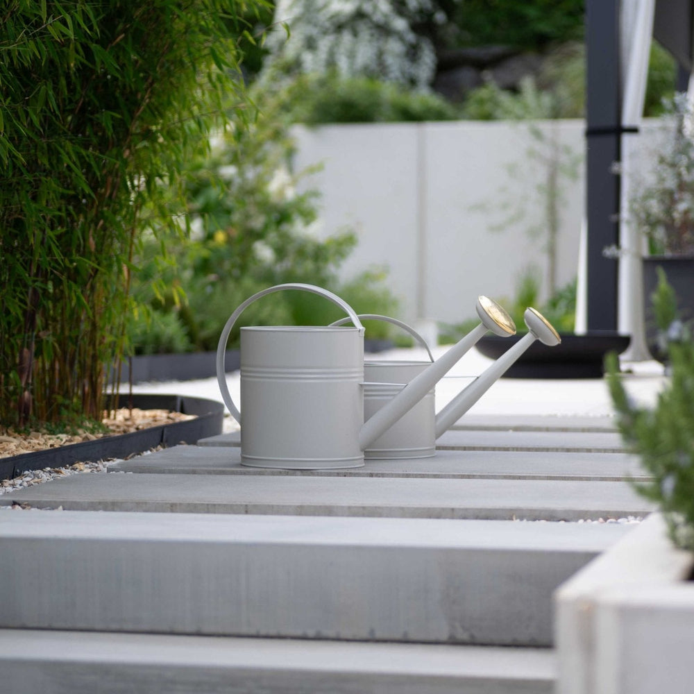Metall Gießkanne 10L von LIVLIG, in Grau, mit goldenem Brausekopf auf grauen Betonplatten.
