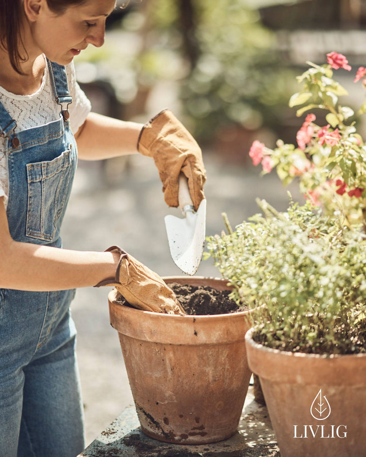 a woman in overalls and gardening gloves is shoveling dirt into a potted