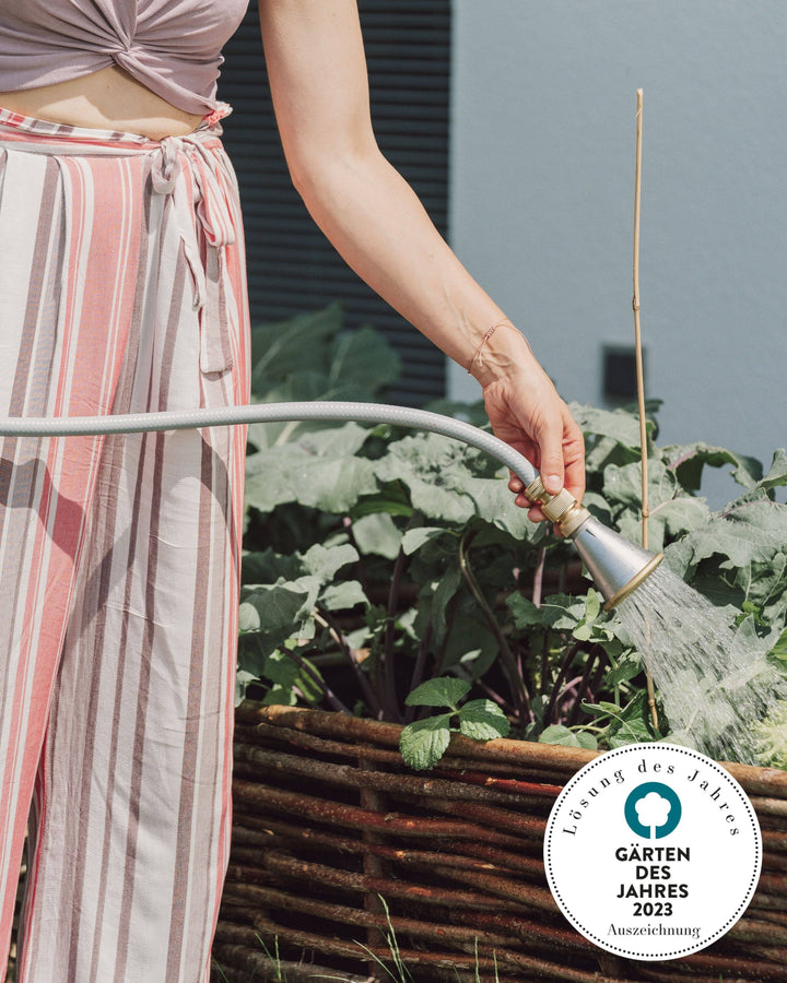 a woman watering plants with a garden hose