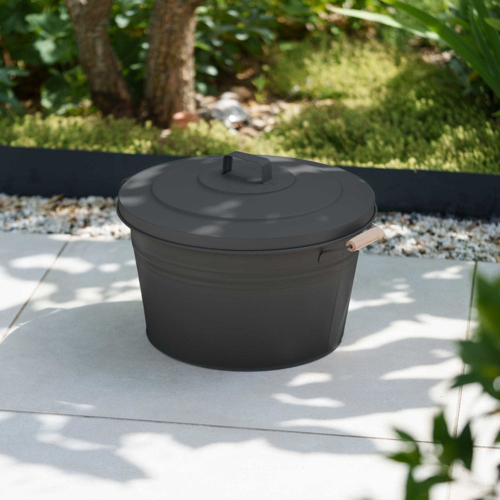 Schlauchtopf aus Metall von LIVLIG, mit Deckel und Holzgriff, im Garten platziert.