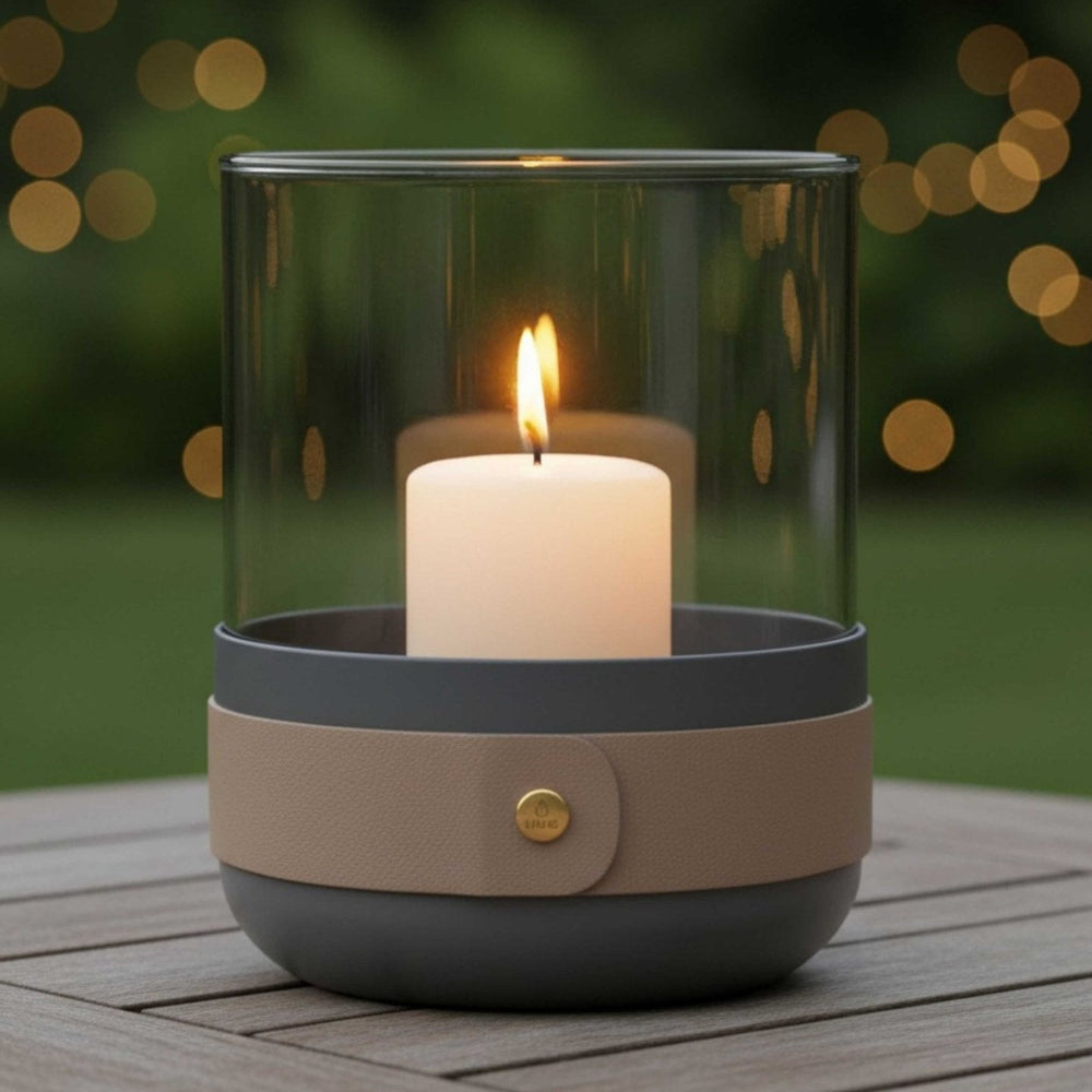 Design Windlicht von LIVLIG mit Glaszylinder und Lederband auf einem Holztisch, im Hintergrund Bokeh-Lichter.
