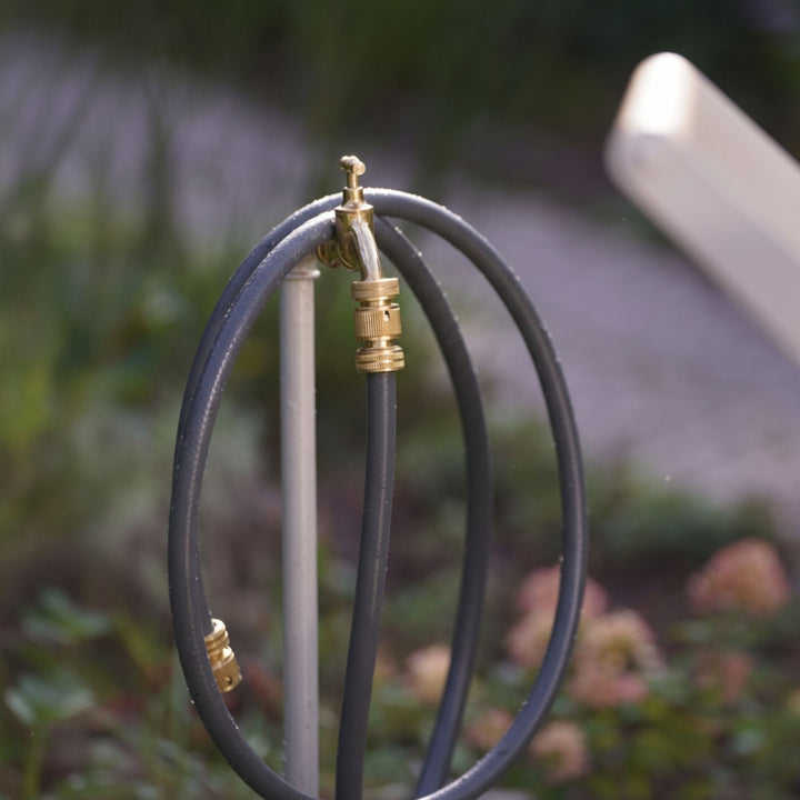 Anschlussgarnitur Gartenschlauch 2m von LIVLIG, zusammengerollt um einen Wasserhahn im Garten.