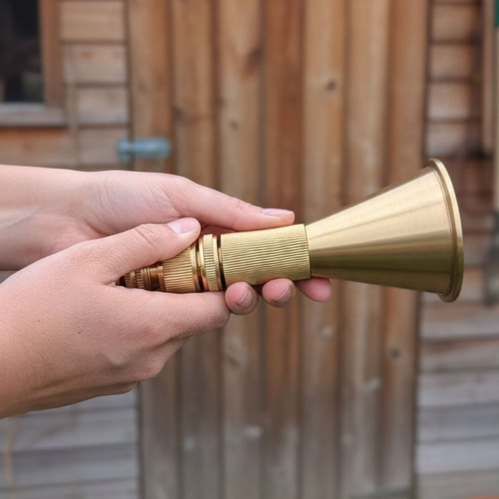 Hands holding a brass-colored cone-shaped object with ribbed grip, against blurred wooden background.