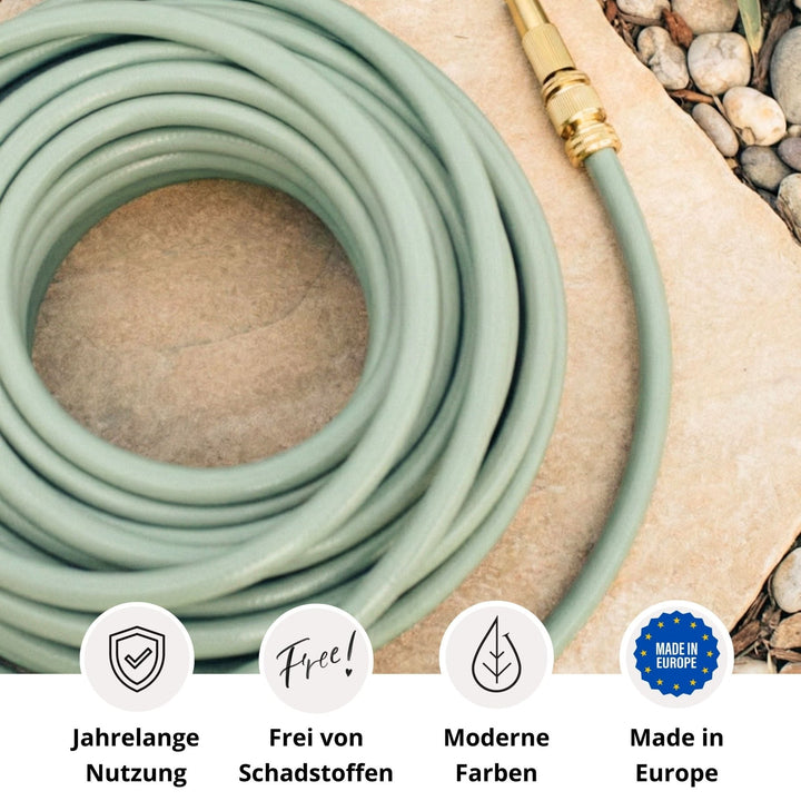 Grüner Design-Gartenschlauch von LIVLIG, aufgerollt auf einer Steinplatte, mit goldenen Verbindungsstücken und umgeben von Steinen.
