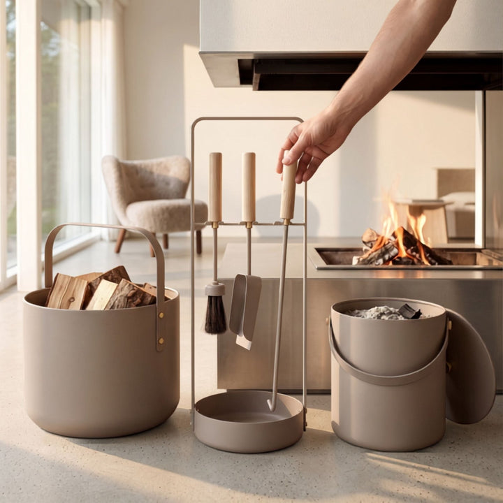 Elegantes Kaminbesteck in taupe mit Holzgriffen von LIVLIG, im Lifestyle-Setting vor brennendem Kamin, mit passenden Eimern für Holz und Asche.