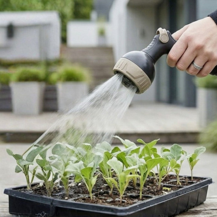Beige flexible garden hose nozzle with spray function watering seedlings in tray, close-up lifestyle view