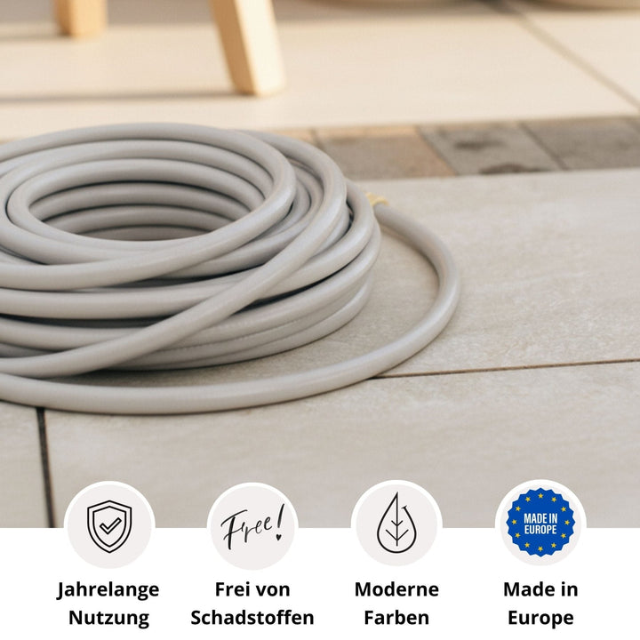 Grauer Gartenschlauch von LIVLIG, aufgerollt auf Fliesenboden, mit Logos für lange Nutzungsdauer, Schadstofffreiheit, moderne Farben und Herstellung in Europa.
