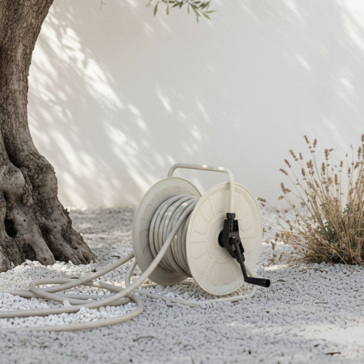 Greiger Gartenschlauch Set mit Trommel von LIVLIG auf Kieseln, umgeben von Olivenbaum und Pflanzen.