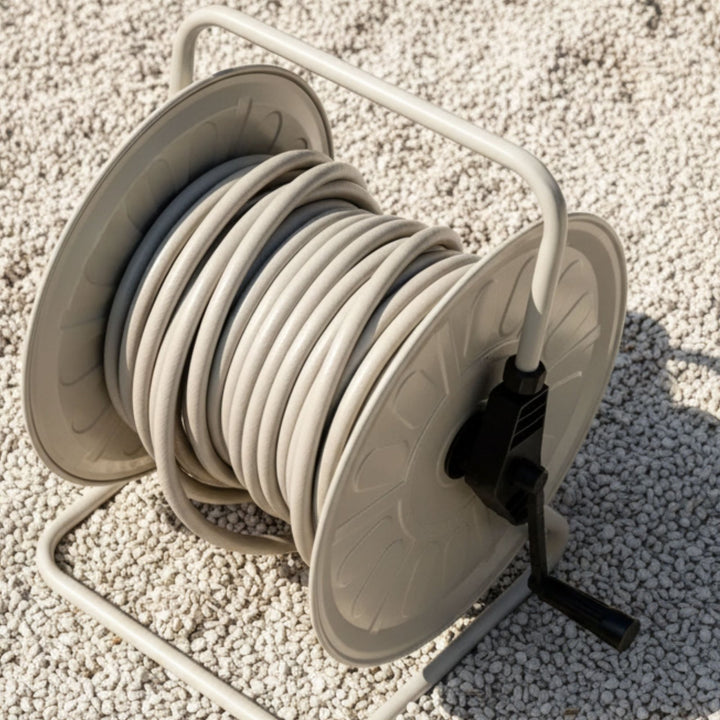 Gentle Greige Gartenschlauch-Set von LIVLIG auf einer Trommel mit schwarzer Kurbel, auf hellem Kiesuntergrund.