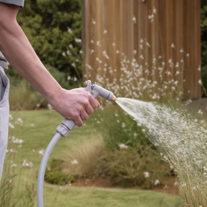 Gartenschlauch Set in sanftem Greige von LIVLIG, dessen Sprühdüse von einer Hand im Garten gehalten wird und Wasser spritzt.
