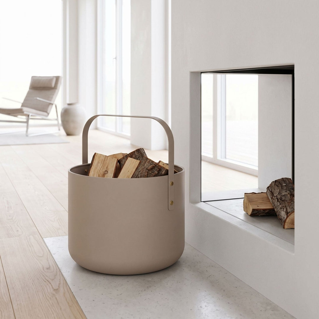 Beige Metallkaminholzkorb von LIVLIG mit integriertem Griff, gefüllt mit Holzscheiten, im modernen Wohnraum vor Kamin platziert