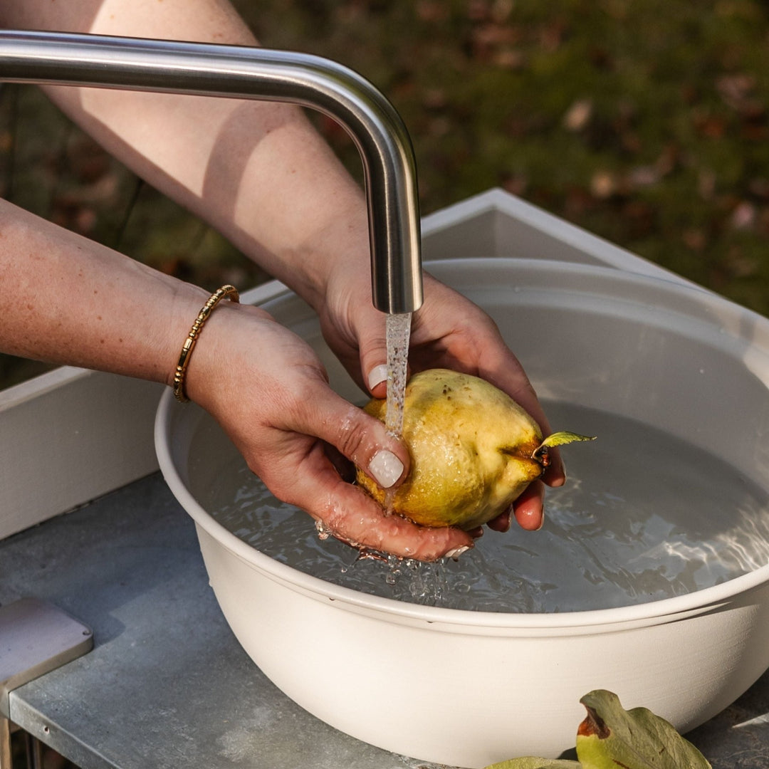 Wasserhahn für die Outdoorküche von LIVLIG, unter dem eine Quitte in einem Waschbecken gewaschen wird.
