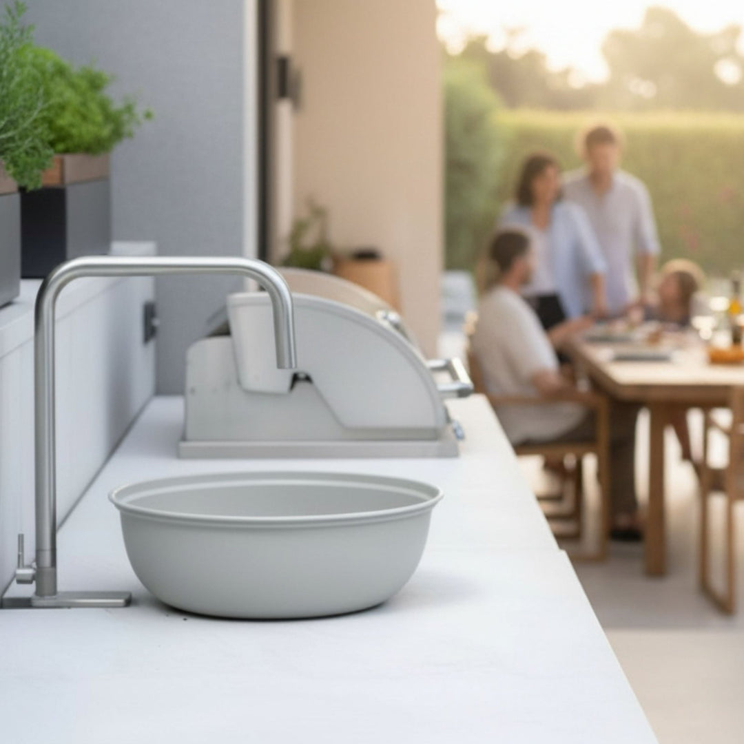 Moderner silberner Wasserhahn von LIVLIG in einer Outdoorküche mit Schüssel und unscharfen Personen im Hintergrund.