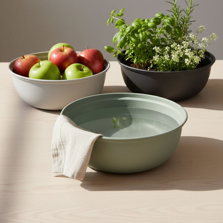 Grüne Pflanzschale bzw. Waschschüssel von LIVLIG, mit Wasser gefüllt und einem Tuch, neben Äpfeln und Kräutern.