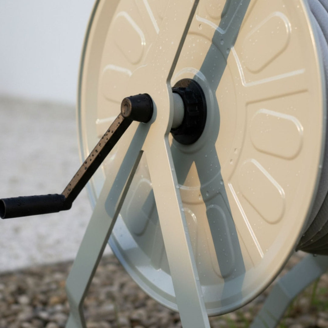 Schlauchwagen Komplettset in sanftem Greige von LIVLIG mit schwarzer Kurbel und sichtbaren Wassertropfen auf der Trommel, Nahaufnahme.