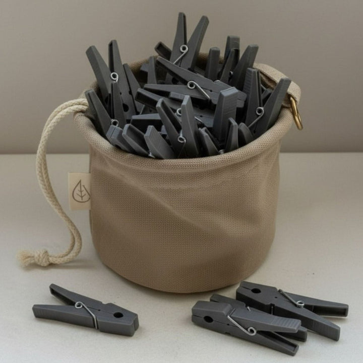 Beiger Wäscheklammerbeutel mit grauen Wäscheklammern von LIVLIG, mit Kordelzug und Label mit Blatt-Symbol.