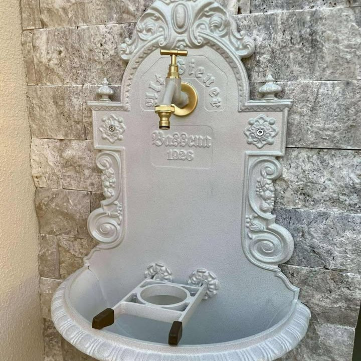 Rosettengarnitur von LIVLIG, hellgrau mit goldenem Hahn, dekorativem Relief und floralen Ornamenten an einer Steinwand.